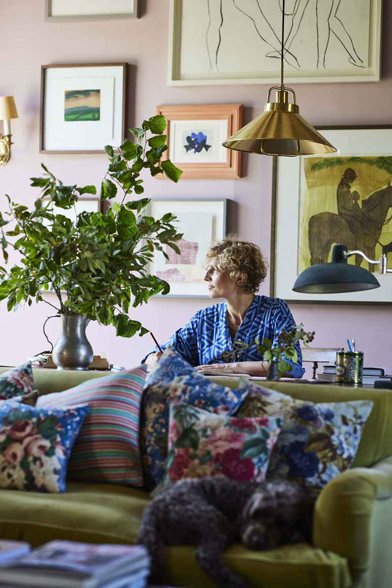 Person sitting on a couch in a colorful living room with plants and framed artwork, dog resting in the foreground.