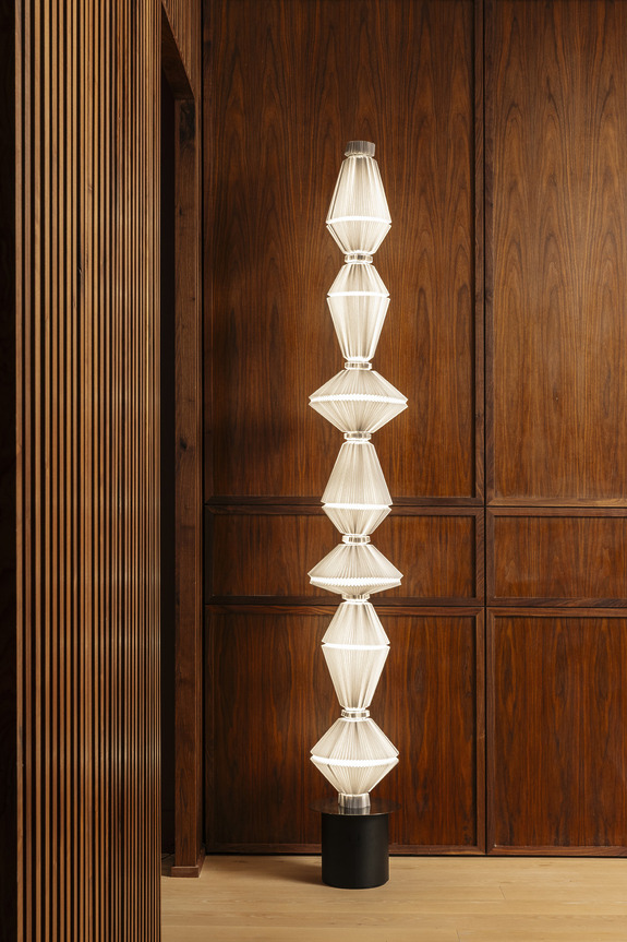 Tall modern floor lamp with geometric white shades, set against a wooden wall background.