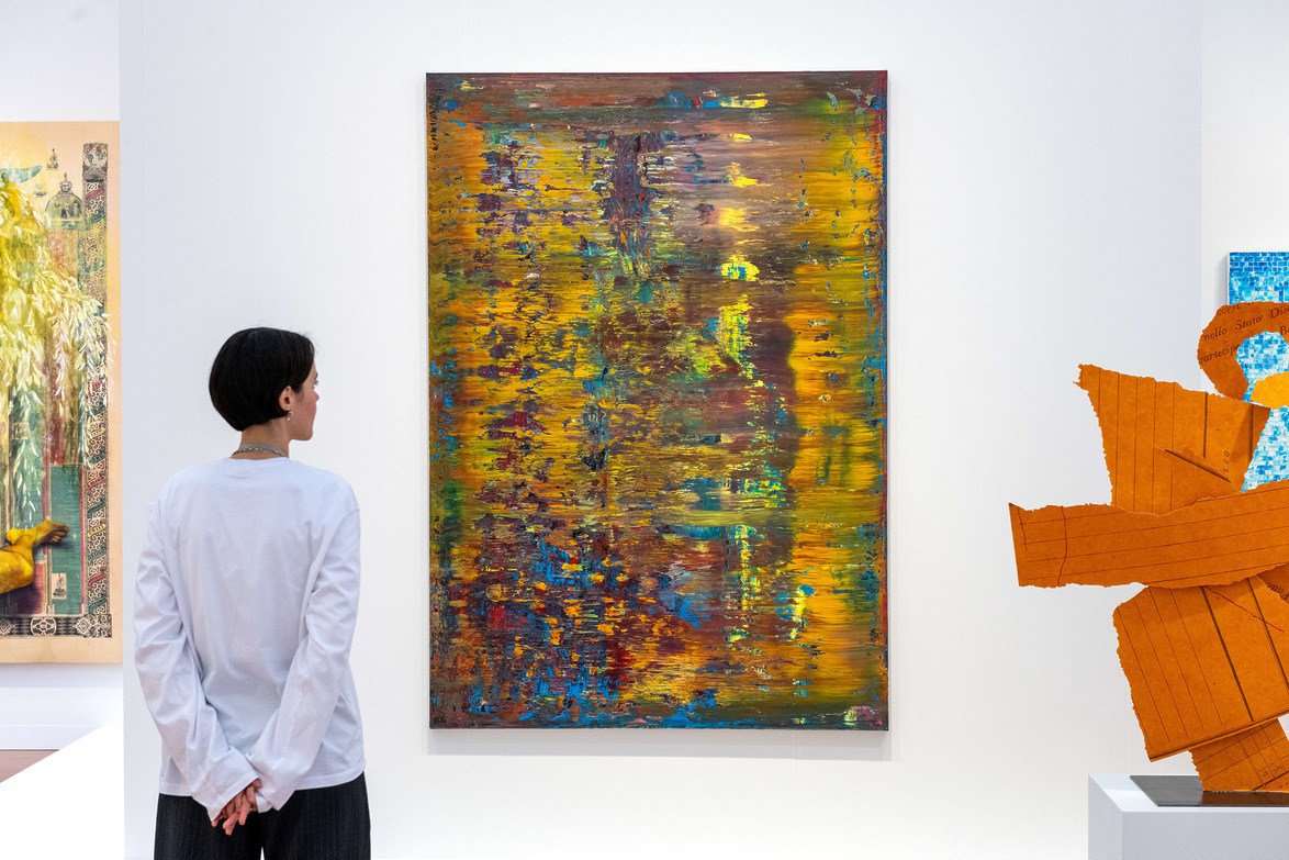 Person looking at a colorful abstract painting in an art gallery with sculptures displayed nearby