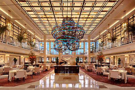 Elegant restaurant interior with a grand light fixture, modern decor, neatly arranged tables, and large windows letting in natural light.