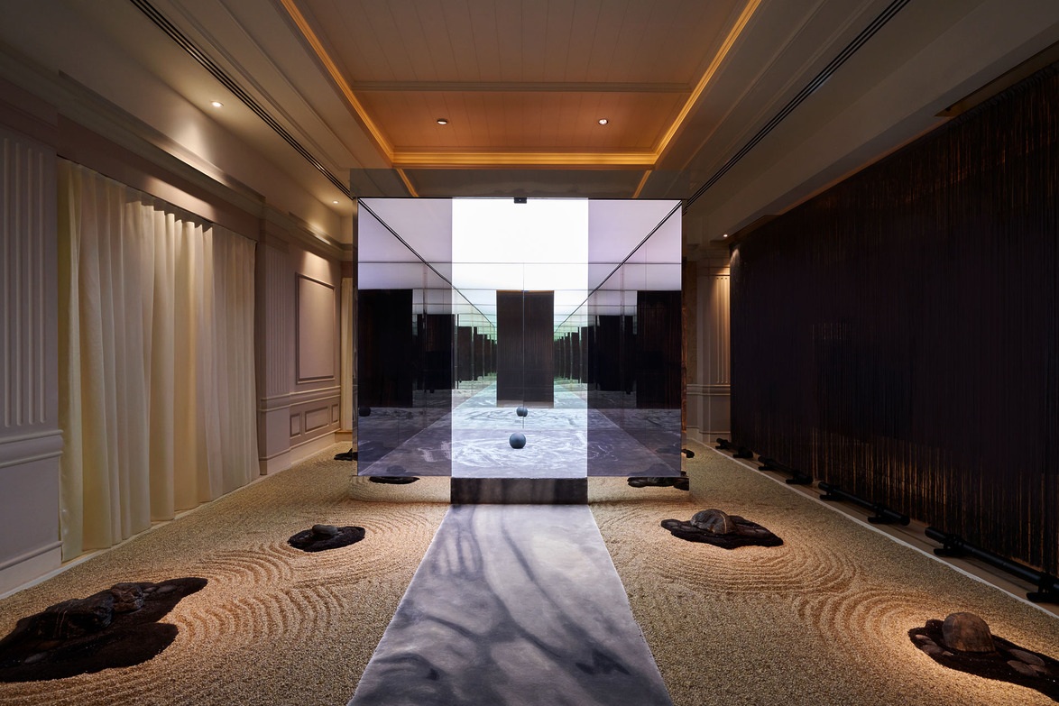 Modern interior with central glass display, sand and stone arrangements, and warm lighting creating a serene ambiance.