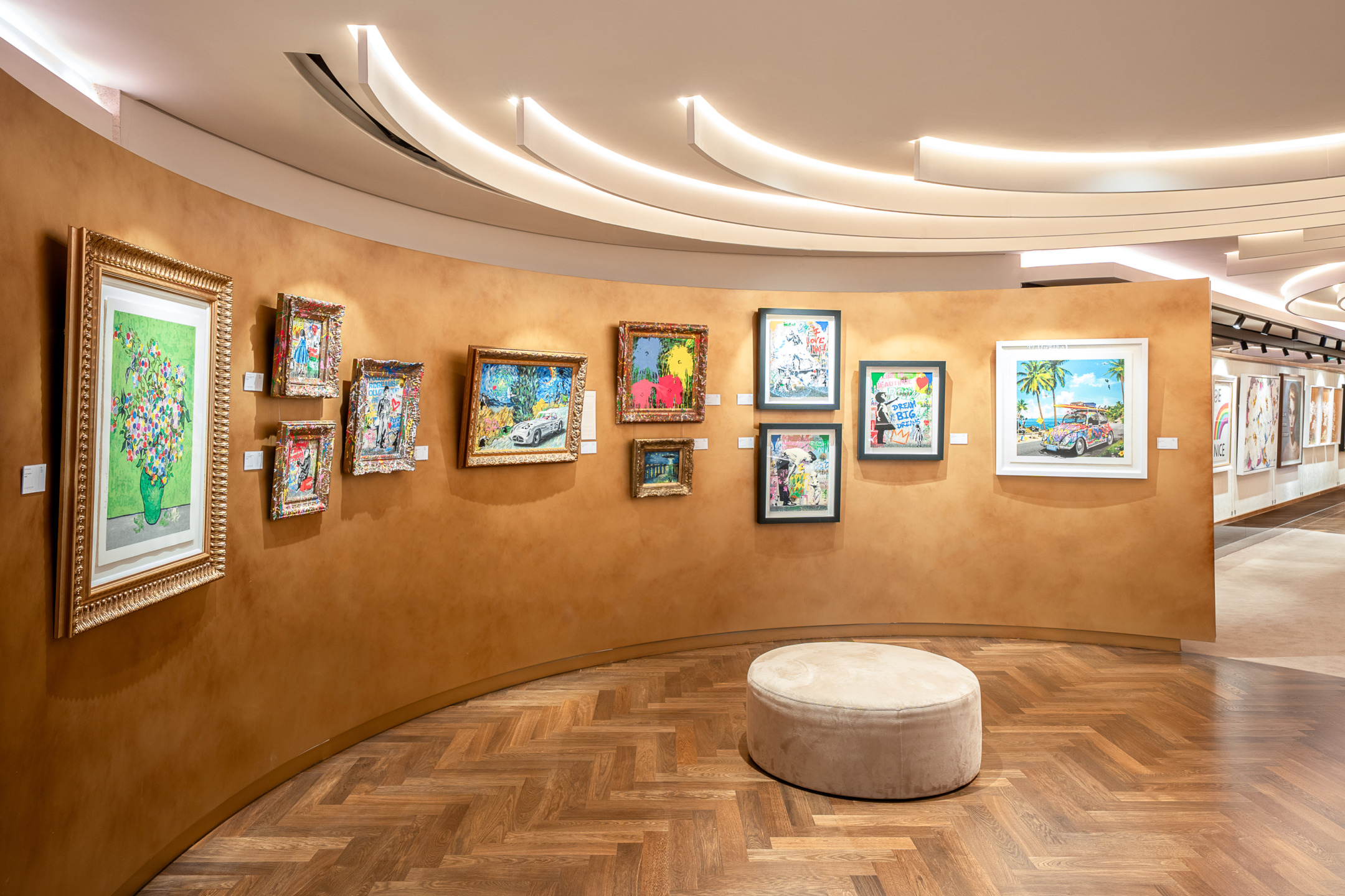 Art gallery interior with various colorful framed paintings on a curved wall and a circular bench on a wooden floor.