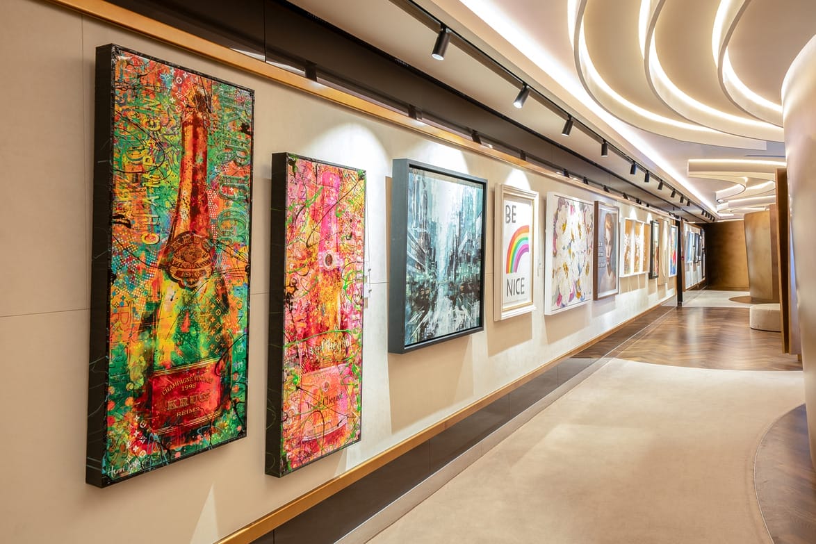 Colorful artwork displayed on a gallery wall with a modern, curving ceiling and track lighting.