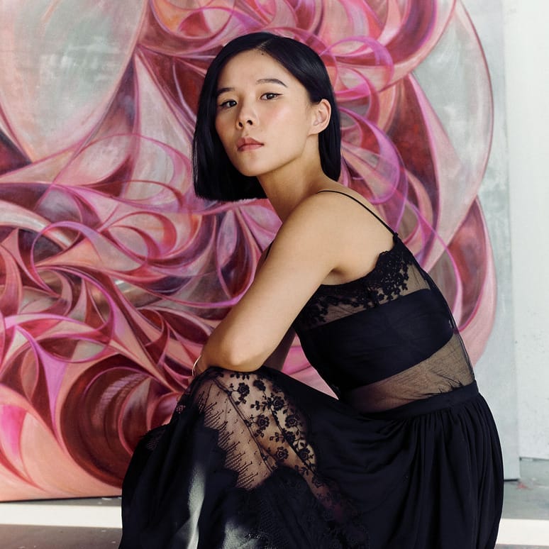 Person in a black dress sits in front of a colorful abstract painting with circular shapes.