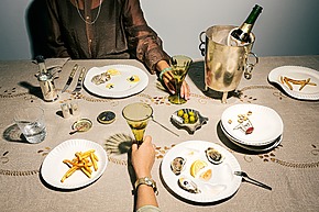 Two people dining with oysters, fries, and champagne on a decorated tablecloth, viewed from above.