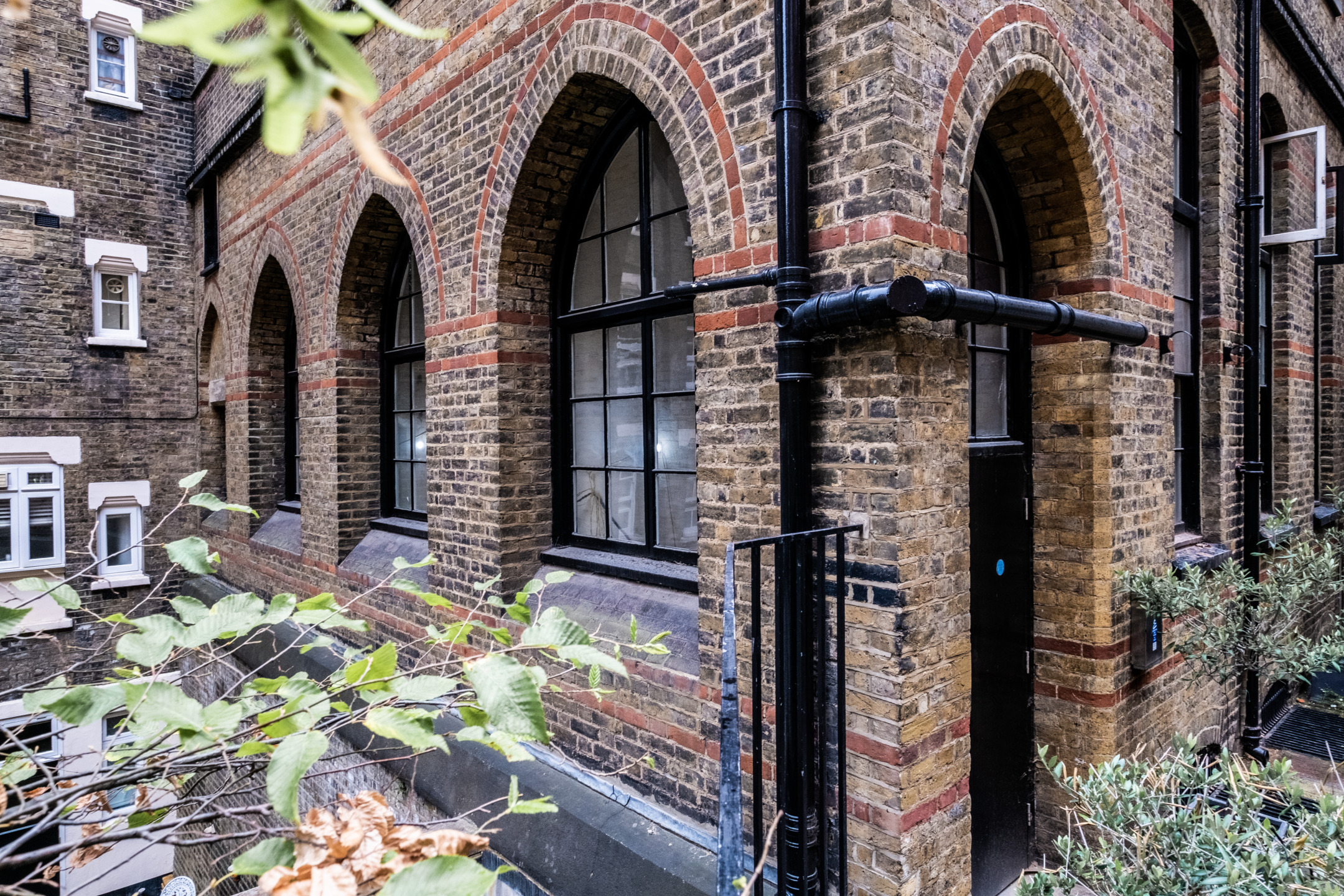 Exterior view of a historic brick building with arched windows and doorway, surrounded by greenery.
