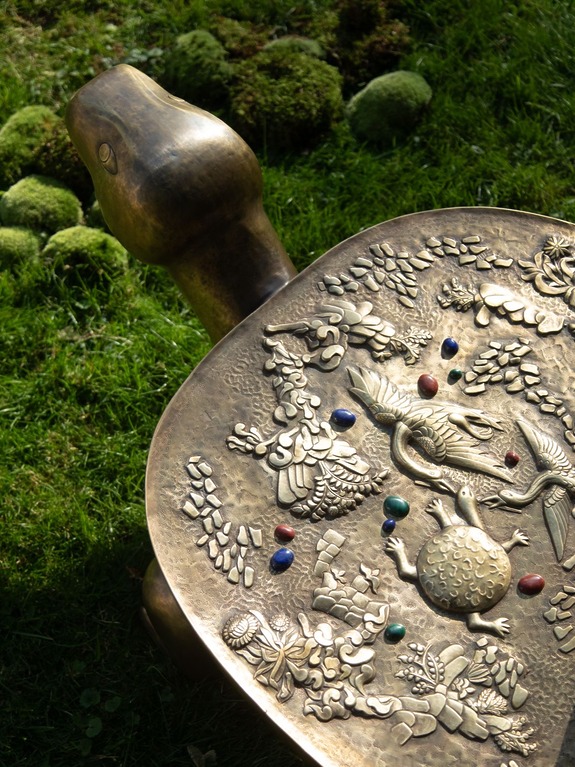 Bronze turtle statue with intricate carvings and colorful stones on its shell, set on green grass with moss.