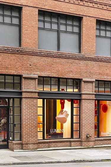 Storefront with large windows displaying modern lighting fixtures against a warm backdrop in a brick building.