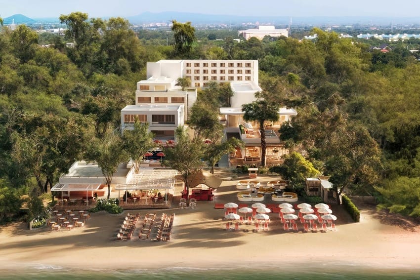 Beachfront resort surrounded by trees, with sun loungers and umbrellas on the sand, overlooking the sea.