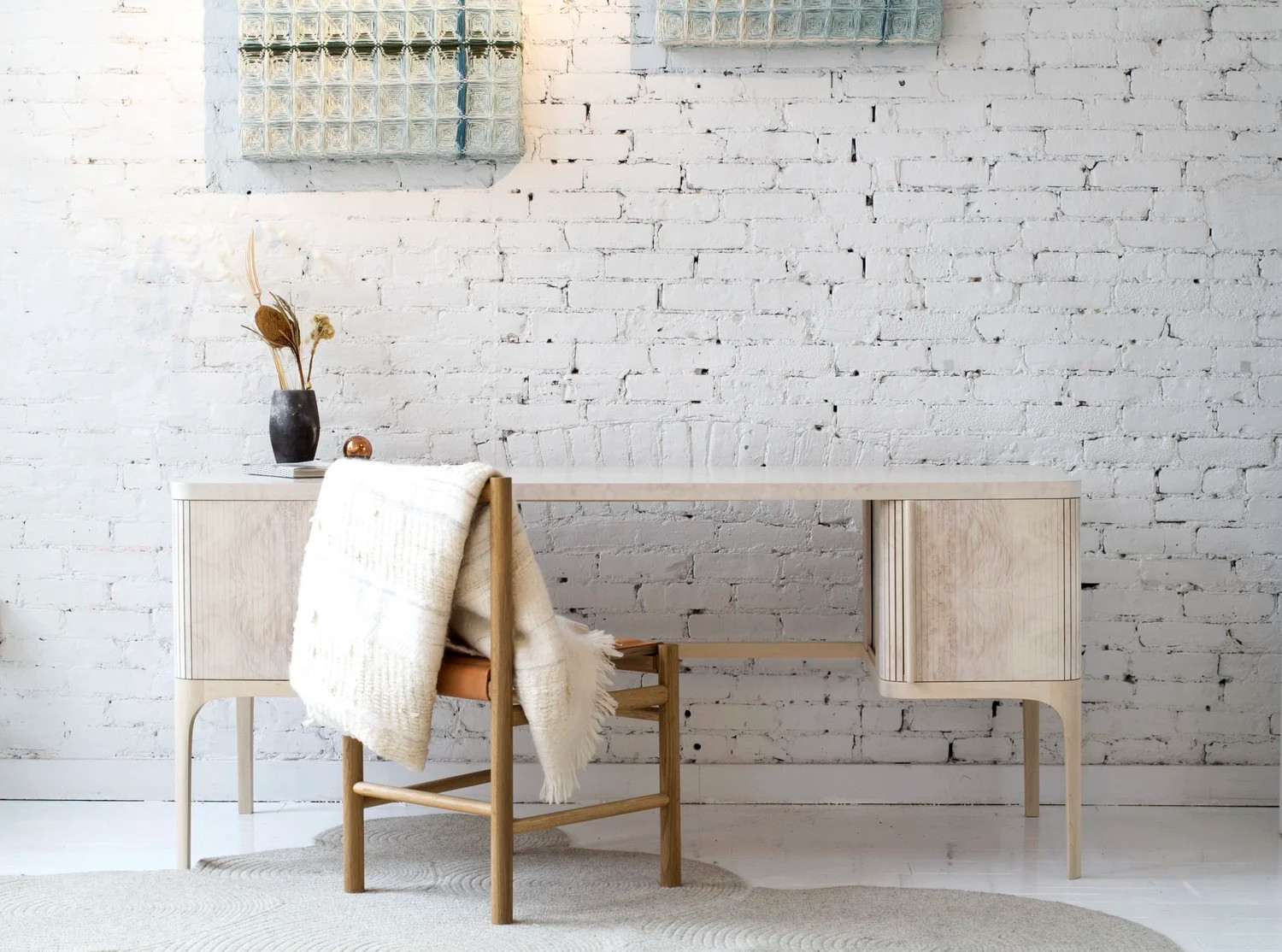 Modern minimalist desk and chair in a bright room with a white brick wall and decorative items.