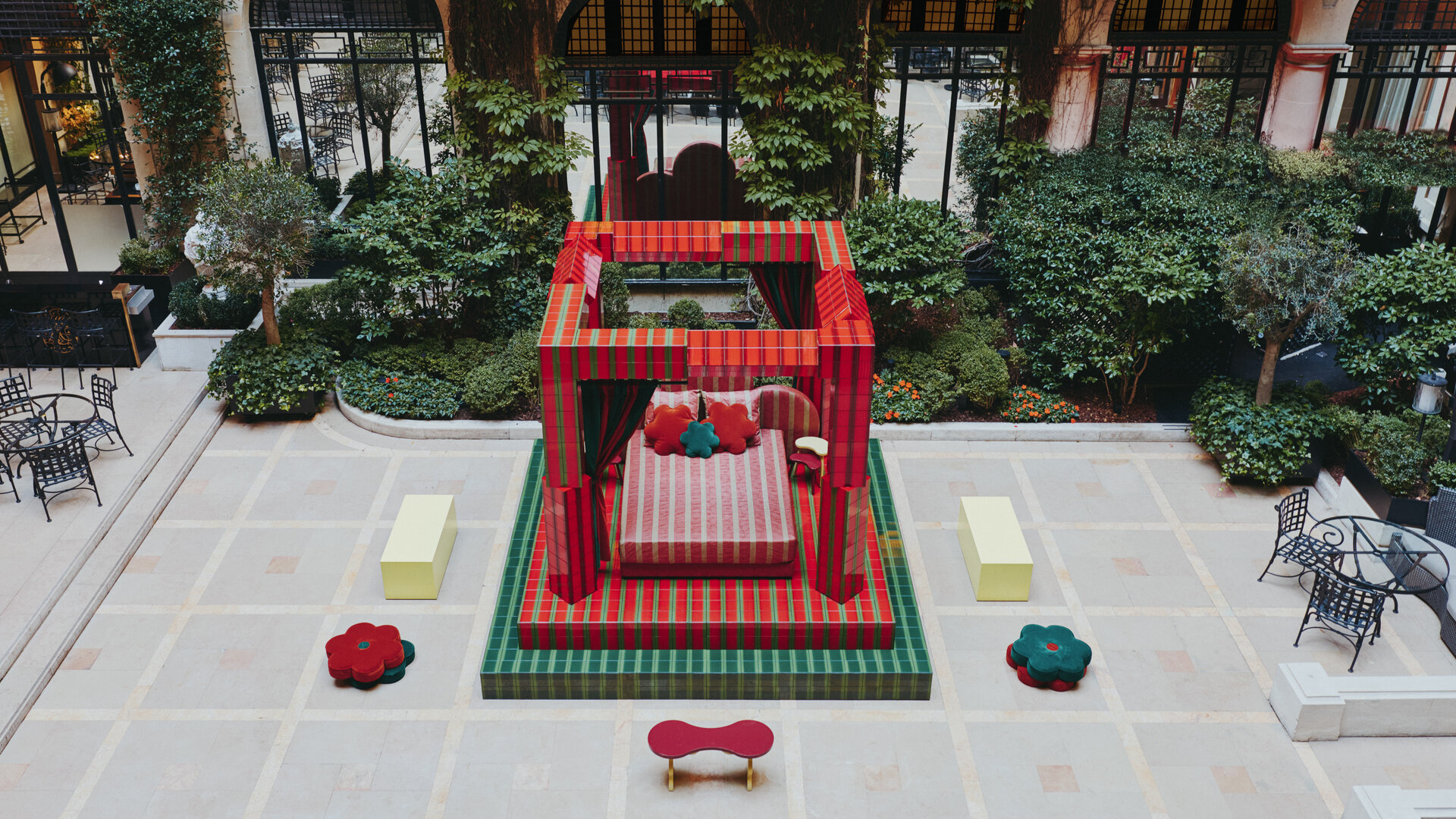 Colorful gazebo-like structure with patterned textiles in a courtyard surrounded by greenery and ornate architecture.