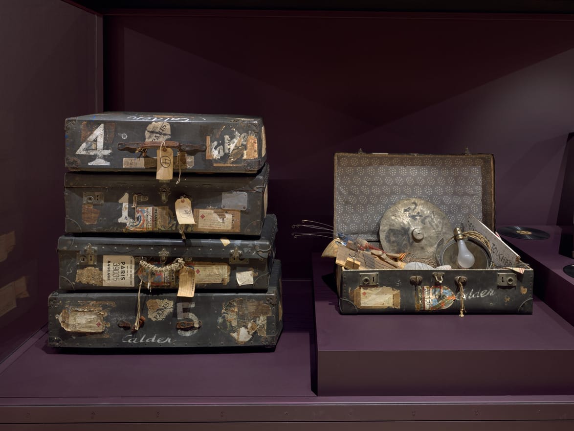 Stack of vintage suitcases, some labeled with numbers and tags, alongside an open suitcase showing various items inside.