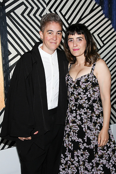 Two people posing together in front of a geometric black and white background.