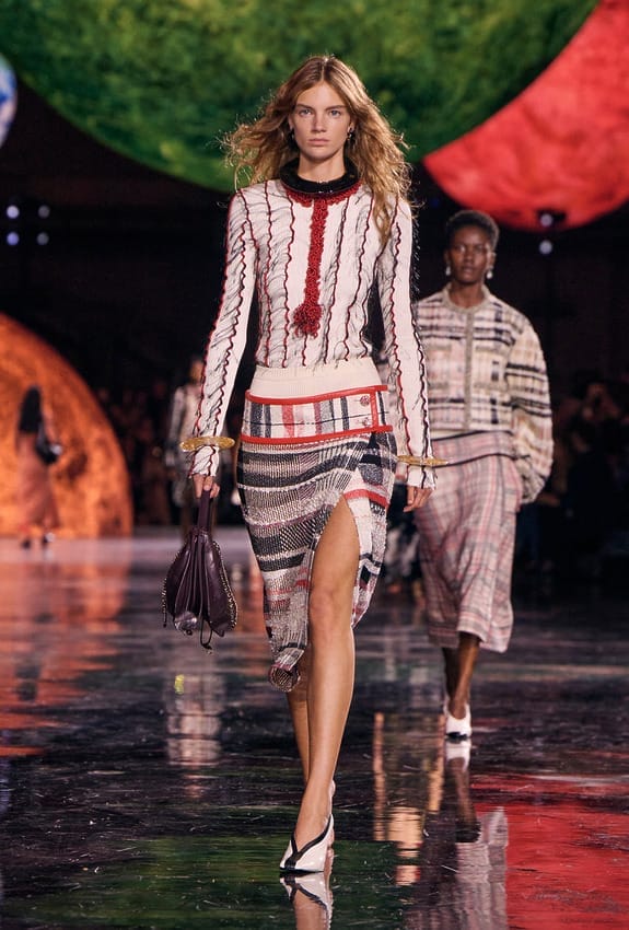 Fashion model in a stylish knit ensemble walking on a reflective runway with vibrant spherical backdrops.