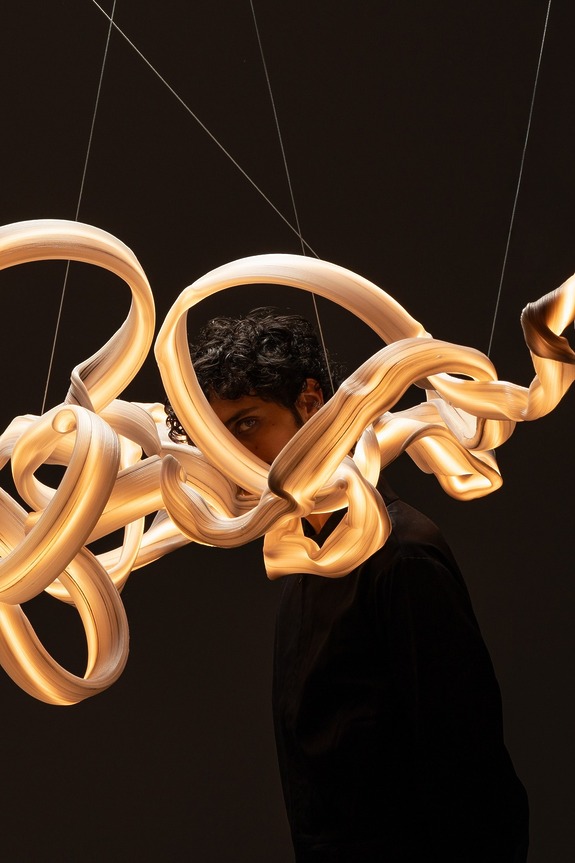 Person partially obscured by intricate, glowing light sculpture against a dark background.