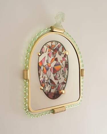 Artistic wall mirror with abstract colorful design, gold accents, and a braided green frame against a neutral background.