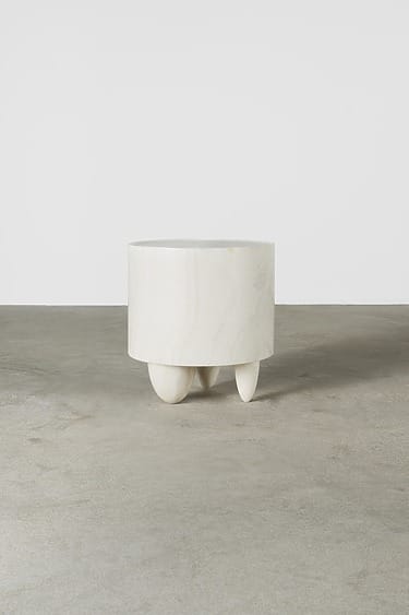 White cylindrical stool with three rounded legs on a concrete floor.