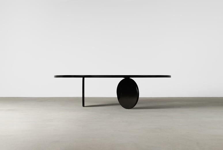 Sleek modern black table with unique circular base on concrete floor against simple white background.