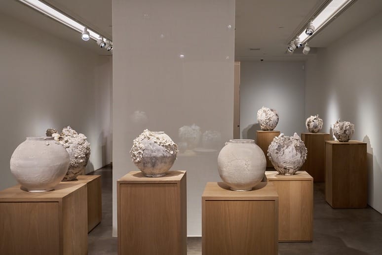Ceramic art exhibition featuring various textured white vases displayed on wooden pedestals in a well-lit gallery setting.