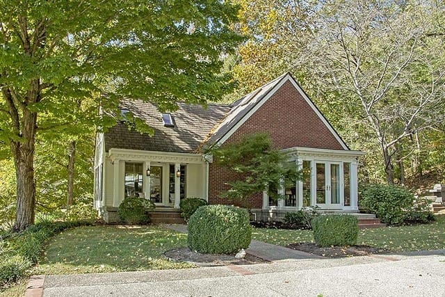 Charming red brick house with large windows surrounded by trees and greenery on a sunny day