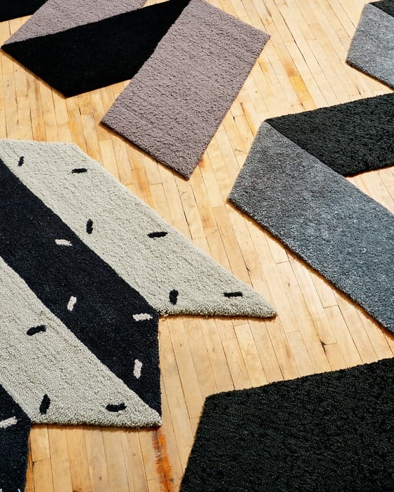 Abstract geometric-patterned rugs on wooden floor with contrasting textures and colors, including black, gray, and beige.