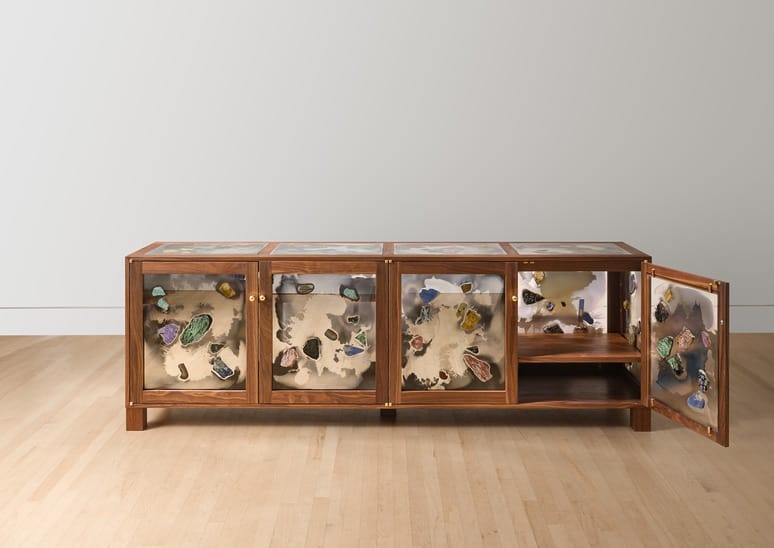 Wooden cabinet with transparent doors displaying various colorful minerals on a light wooden floor.