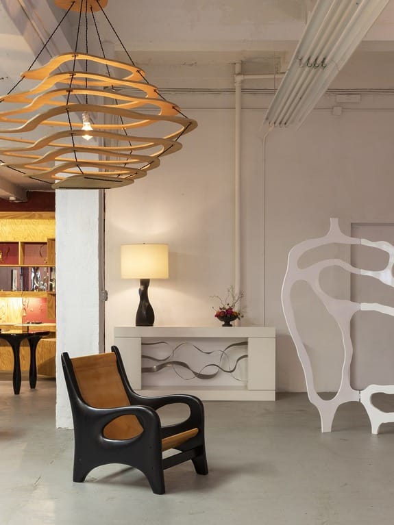 Modern interior with unique wooden chair, abstract lighting, artistic decor, and a warm-lit lamp on a console table.