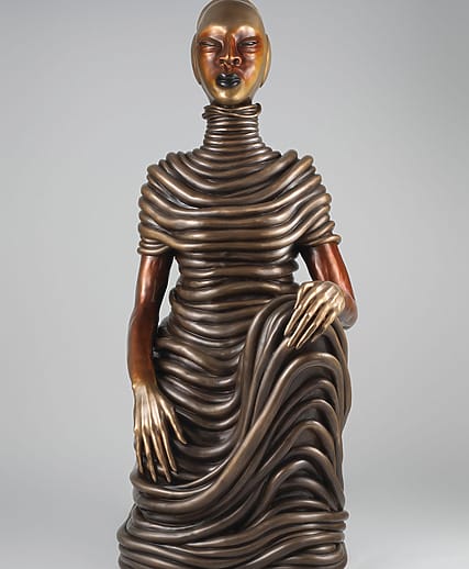 Bronze sculpture of a seated woman wrapped in coiled, textured layers with a serene expression against a neutral background.