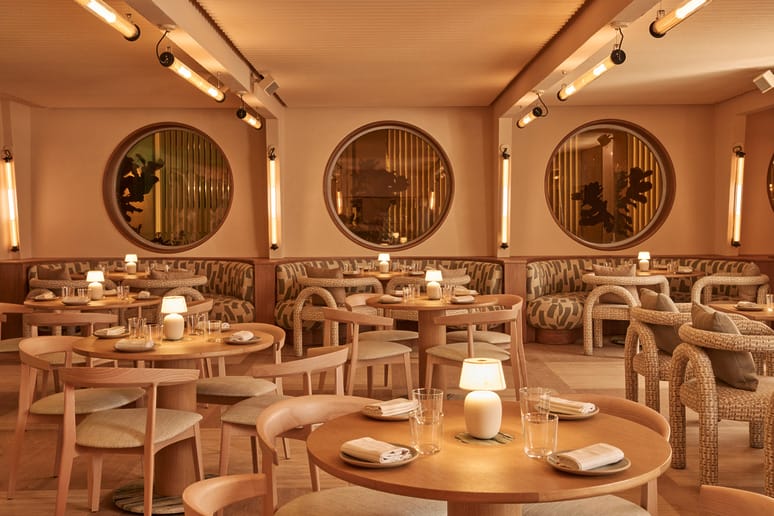 Cozy restaurant interior with round windows, wooden tables, and soft lighting.