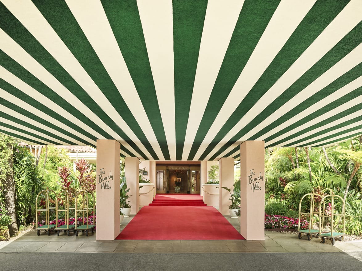 Striped green and white canopy over a red carpet entrance with luggage carts on a sunny day.