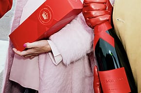 People holding Moët & Chandon gift box and bottle, dressed in winter fashion with red and pink accents.