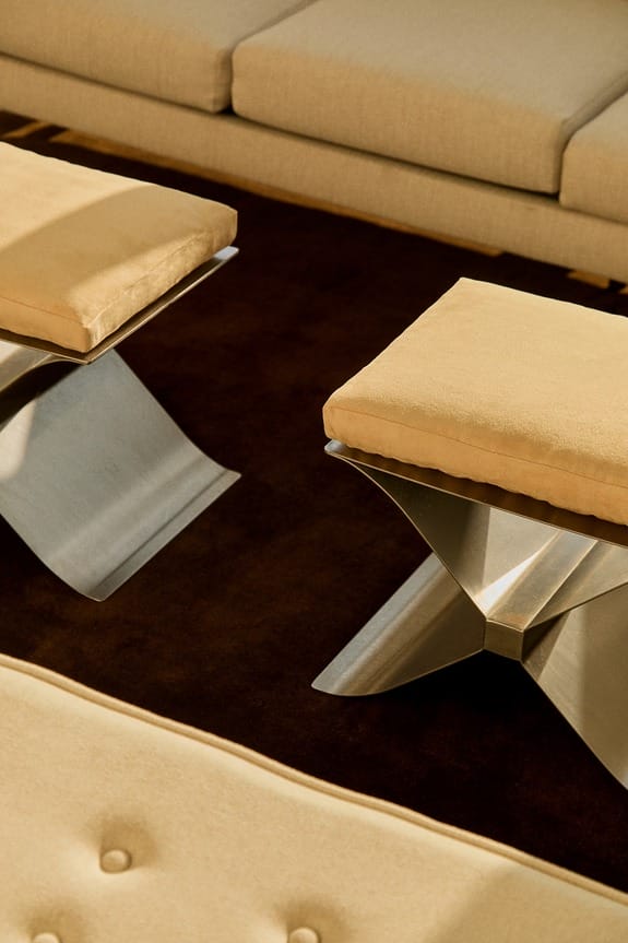 Modern metallic stools with beige cushions on a dark brown floor.
