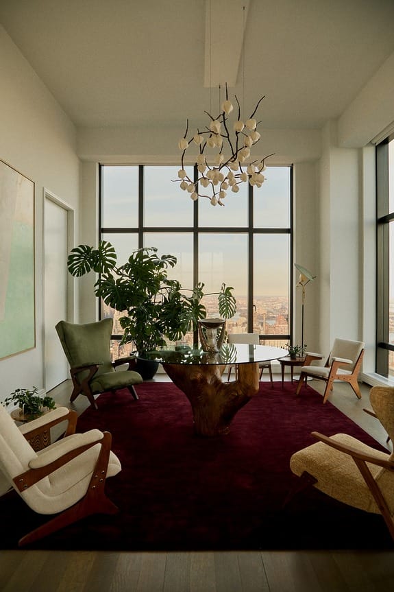 Modern living room with large windows, stylish furniture, green plants, and a unique chandelier on the ceiling.