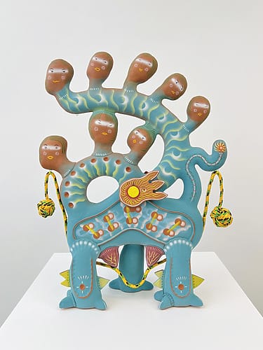 Colorful abstract sculpture with multiple heads and wavy patterns on a pedestal displaying vibrant colors.