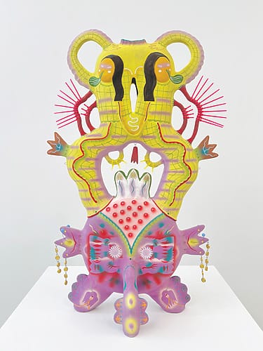 Colorful abstract sculpture with vibrant yellow, pink, and red patterns, intricate designs, and symmetrical shapes on a white base.