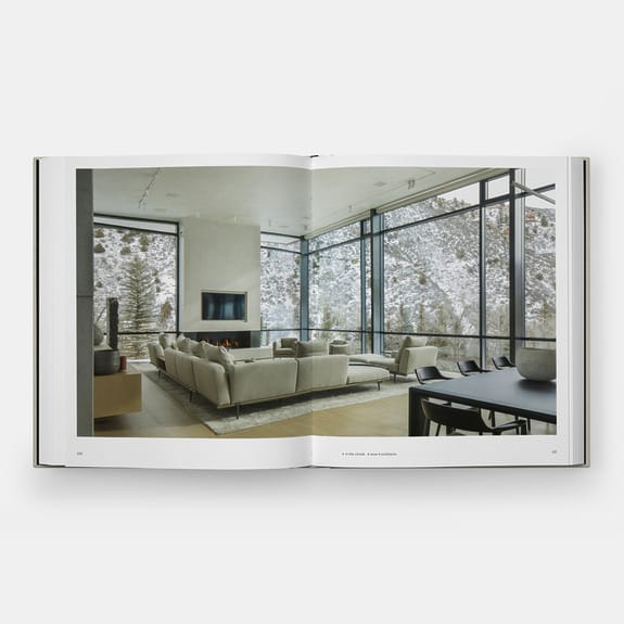 Open book displaying a modern living room with large windows, snowy landscape view, beige sofas, and a wall-mounted TV.