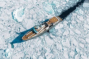 Luxury yacht navigating through Arctic ice floes, top view showing helipad and clear blue sea amidst frozen landscape.