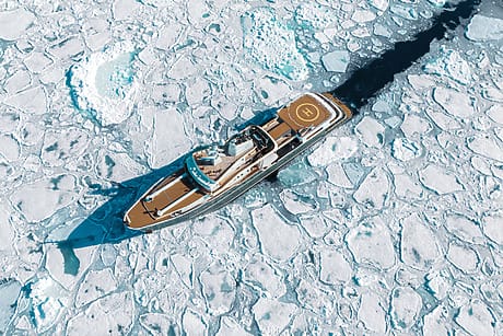 Luxury yacht navigating through Arctic ice floes, top view showing helipad and clear blue sea amidst frozen landscape.