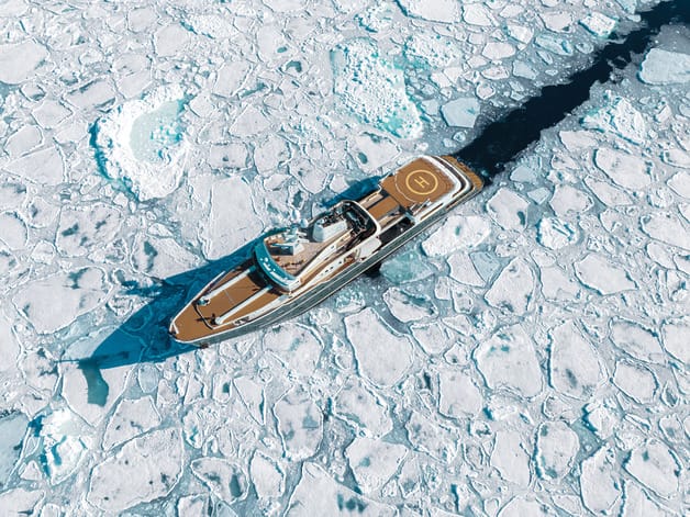 Luxury yacht navigating through Arctic ice floes, top view showing helipad and clear blue sea amidst frozen landscape.