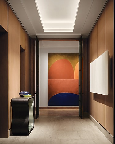 Modern hallway with wooden panels, a colorful abstract painting, curved console table, and a ceiling light fixture.