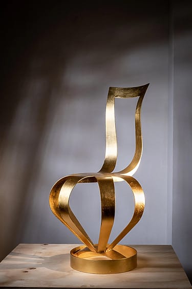 Golden abstract sculpture with twisted ribbon-like design on a wooden surface, set against a dimly lit background.
