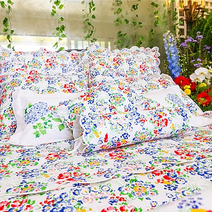 Colorful floral-patterned bed linens with pillows and cushions in a vibrant garden-themed bedroom setting.