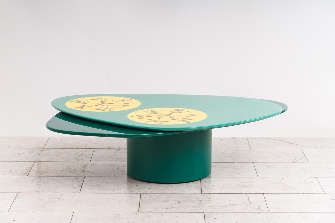Green, oval coffee table with circular yellow inlays, displayed on a light tiled floor against a plain white background.