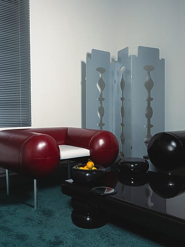 Modern living room with red leather chair, black glossy coffee table, decorative screen, and a bowl of oranges.