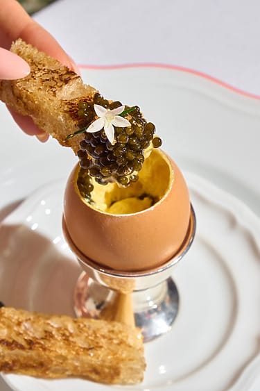 A gourmet dish featuring an eggshell filled with a creamy mixture, topped with caviar and garnished with a delicate flower.