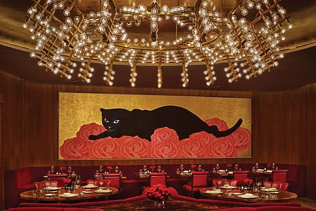 Elegant restaurant interior with a golden ceiling, large chandelier, vibrant artwork of a black panther on roses, and red seating.