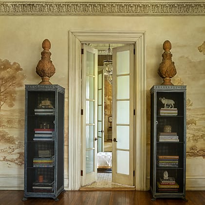 Elegant room with two tall bookshelves flanking open French doors, leading to a bright space with a chandelier in view.
