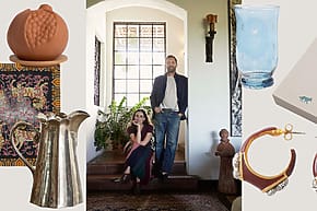 A man and woman pose in a stylish room surrounded by decorative items, including a jug, earrings, and a decorative cloth.