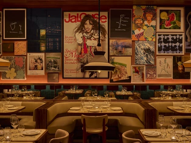 Warmly lit restaurant interior with cushioned booths, vintage posters on the wall, and elegantly set tables.