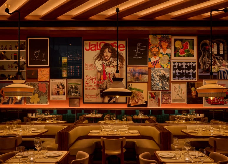 Cozy restaurant interior with elegant table settings and a wall adorned with colorful art and posters.